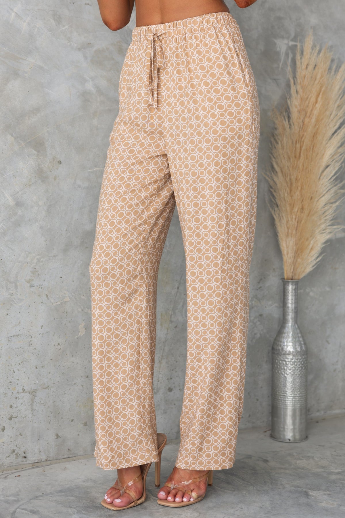 Okar pants in abstract print with mid-high waist, elastic waistband, and pockets, styled with heels.