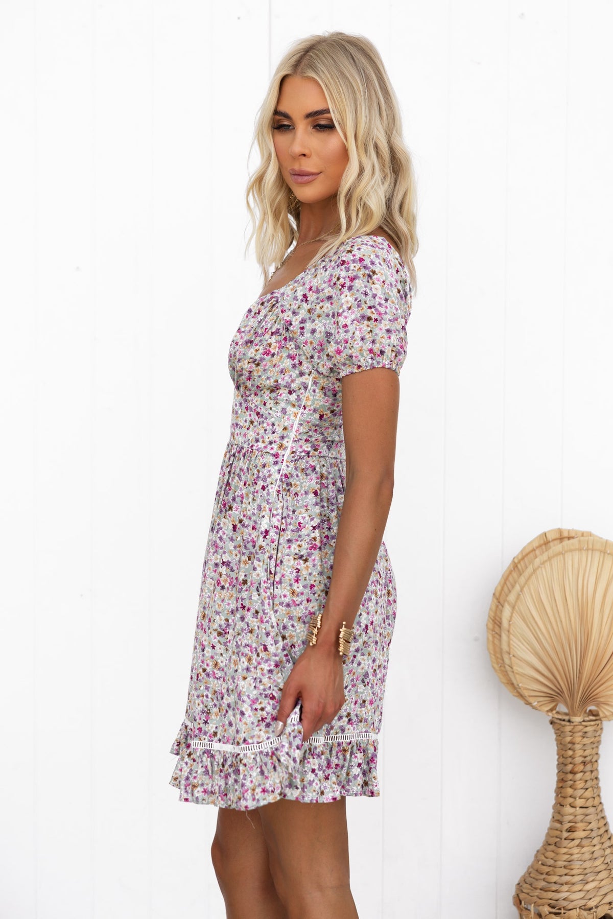 Model in a floral dress featuring short sleeves and ruffled hem, against a white background.