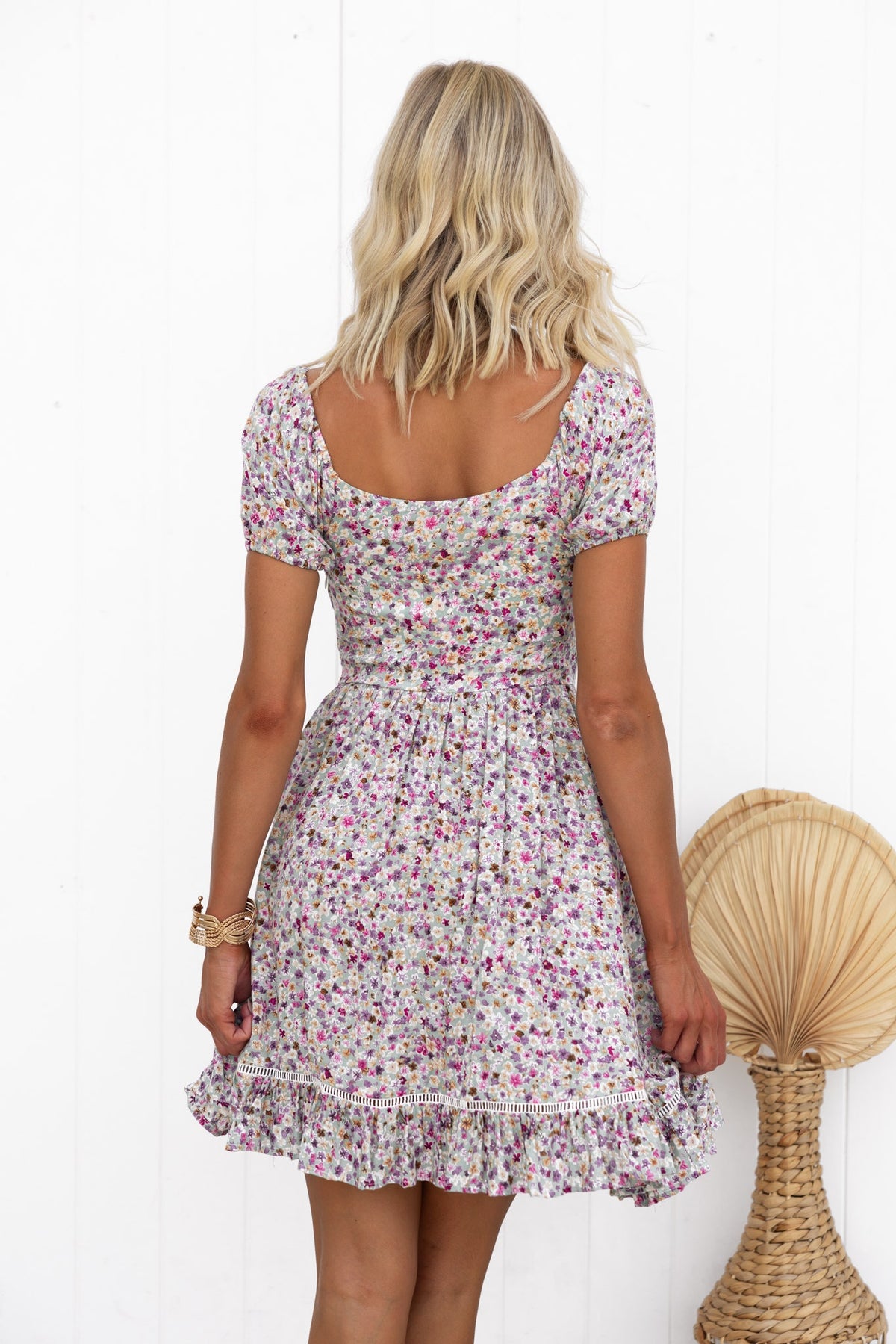Model wearing a floral dress with short puff sleeves, showing the back and ruffled hem.