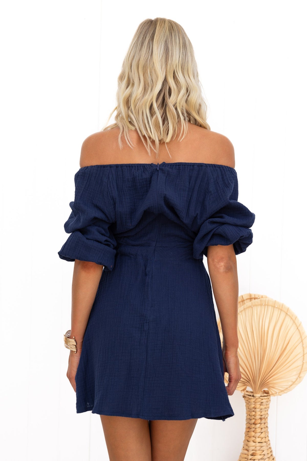 Back view of a navy Mykel Dress featuring an off-shoulder neckline and puff sleeves, styled with beachy waves.