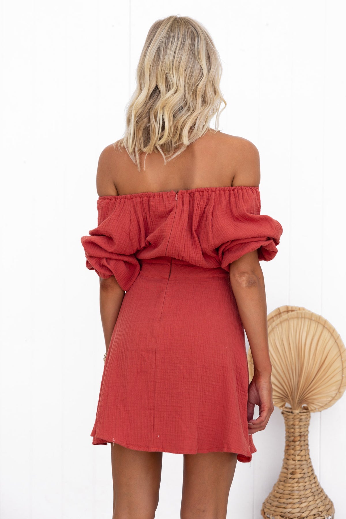 Back view of a woman in a red Mykel dress featuring an off-shoulder neckline and cut-out waist detail.