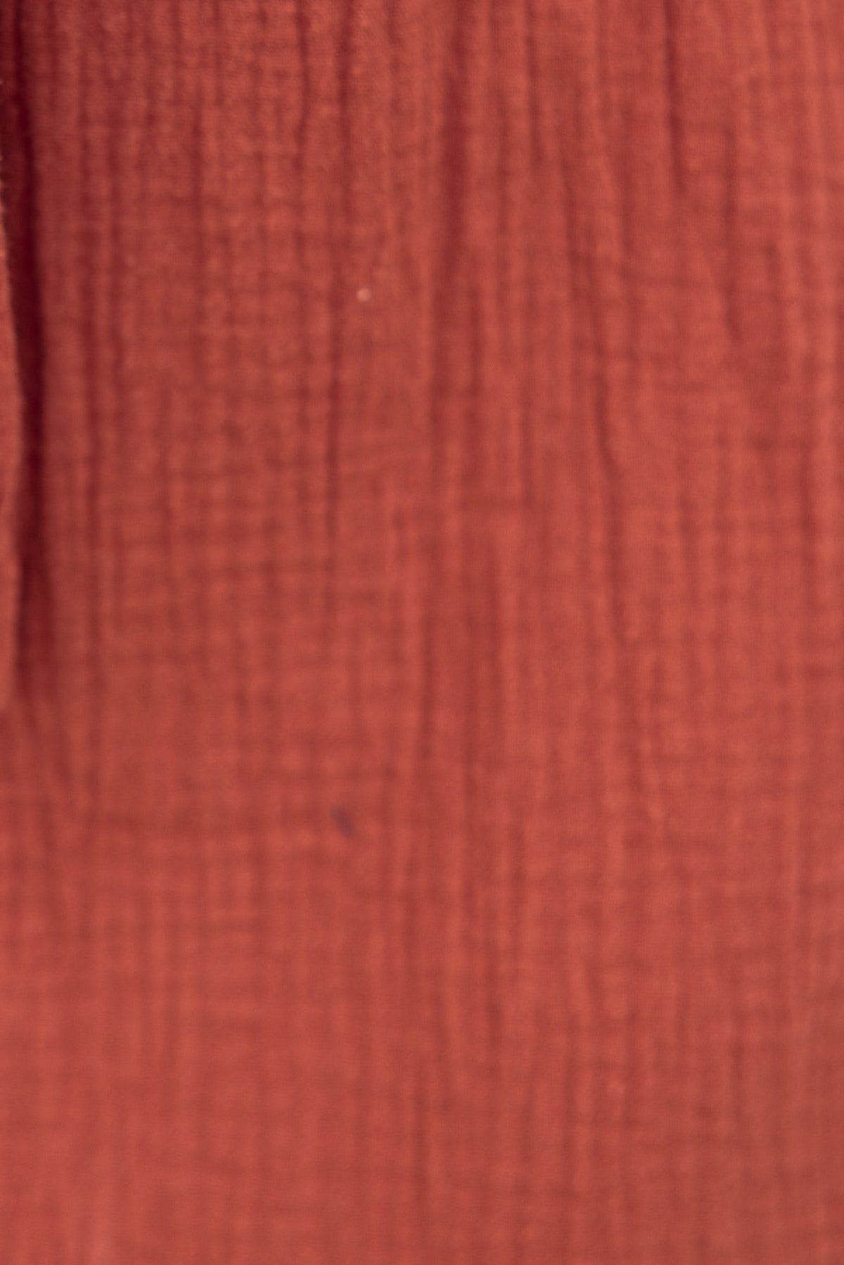 Textured rust-colored fabric close-up, showcasing a soft and lightweight material ideal for summer clothing.