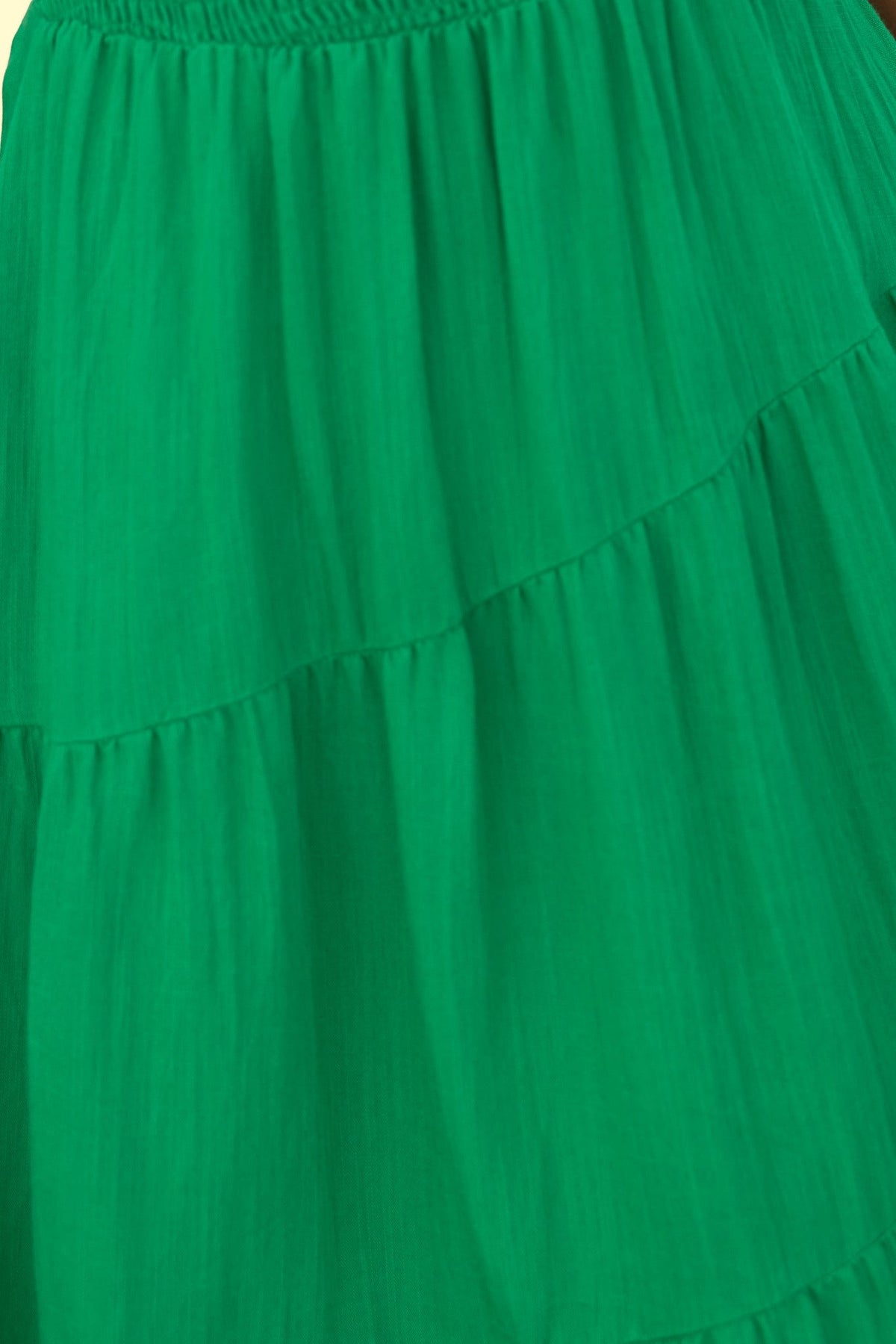 Close-up of vibrant green fabric showcasing tiers of a midi dress skirt, emphasizing softness and texture.