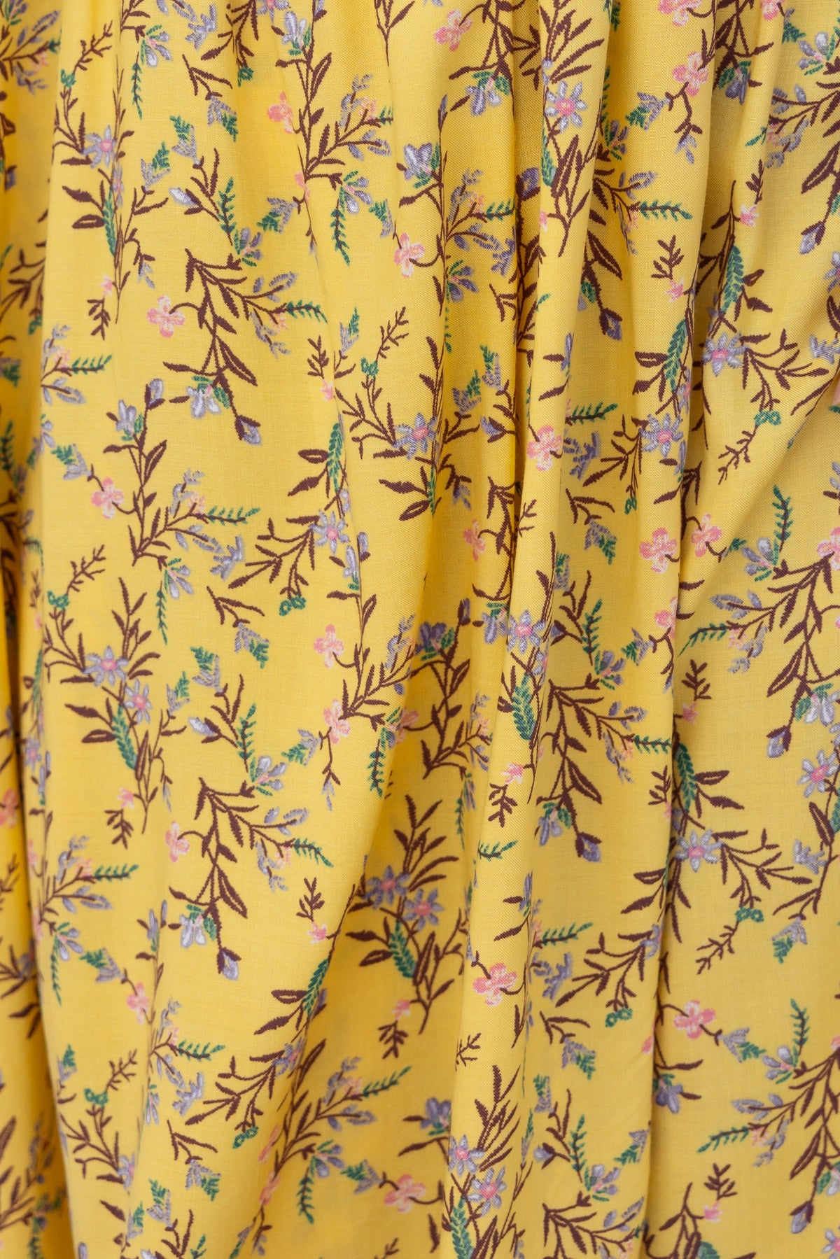 Close-up of floral pattern on yellow fabric, featuring delicate flowers and branches, ideal for a summery midi dress.
