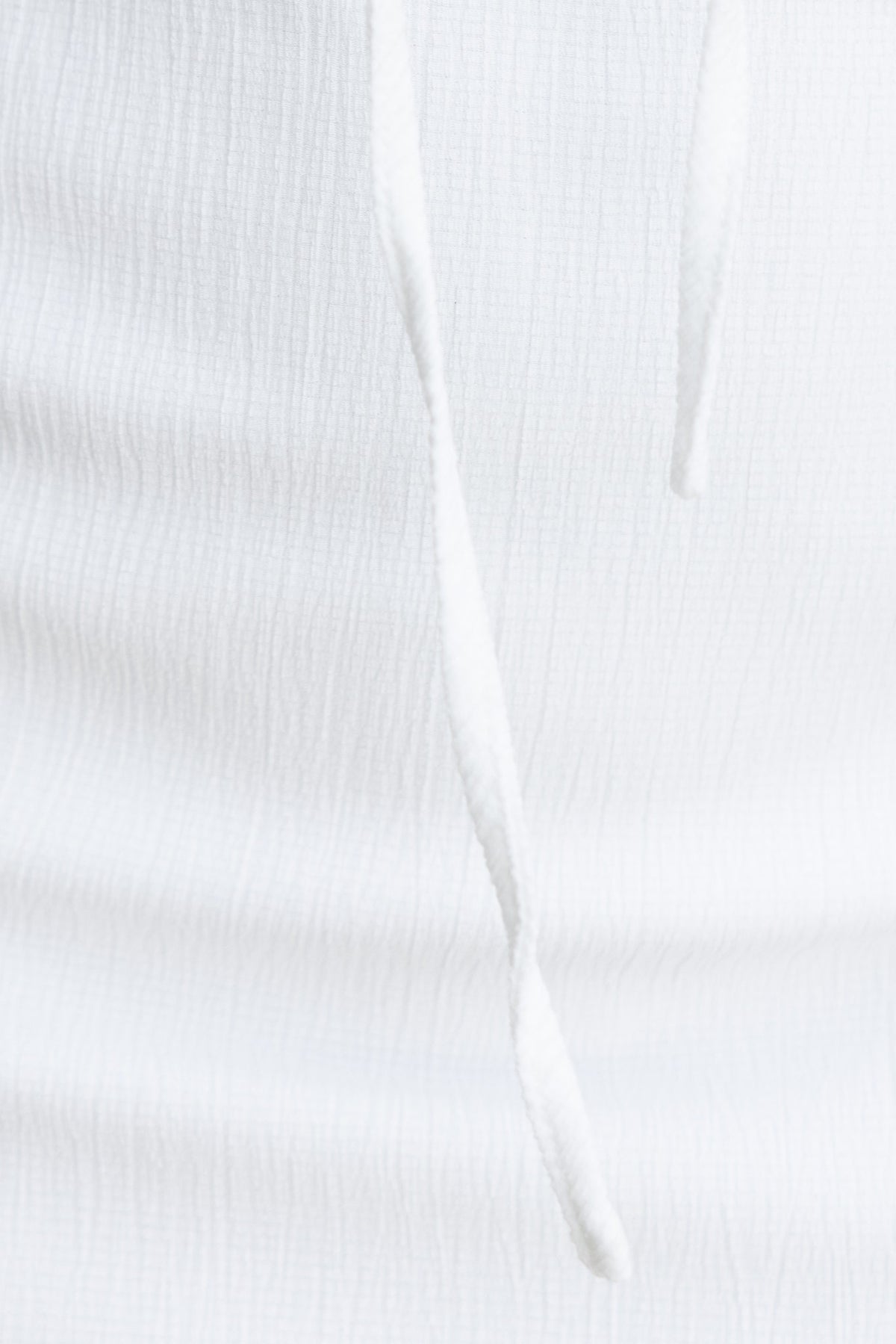 Close-up of textured white fabric with adjustable tie detail from Kolby Dress, highlighting its stylish design.