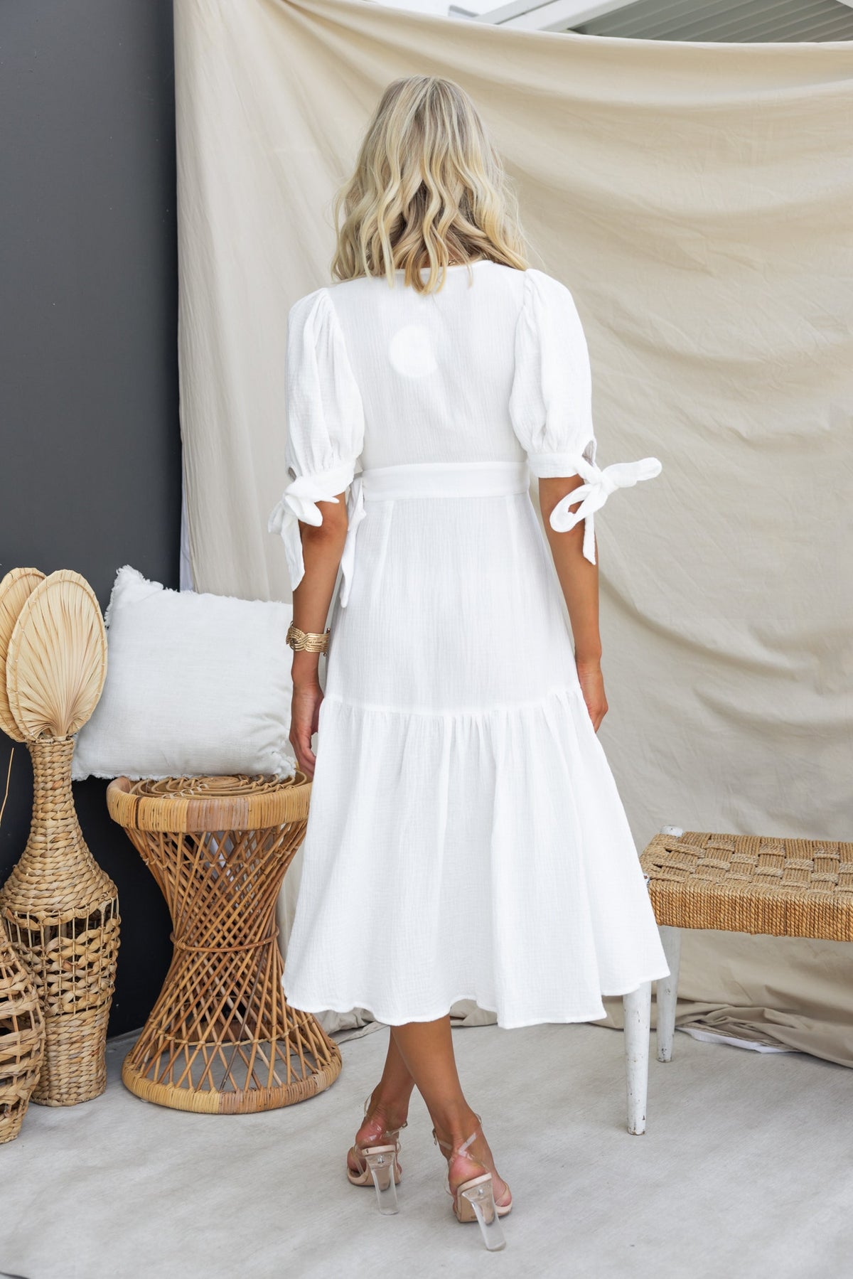 Model wearing the Brunita Wrap Midi Dress from the back, featuring puffy sleeves and a flowing asymmetric hemline.