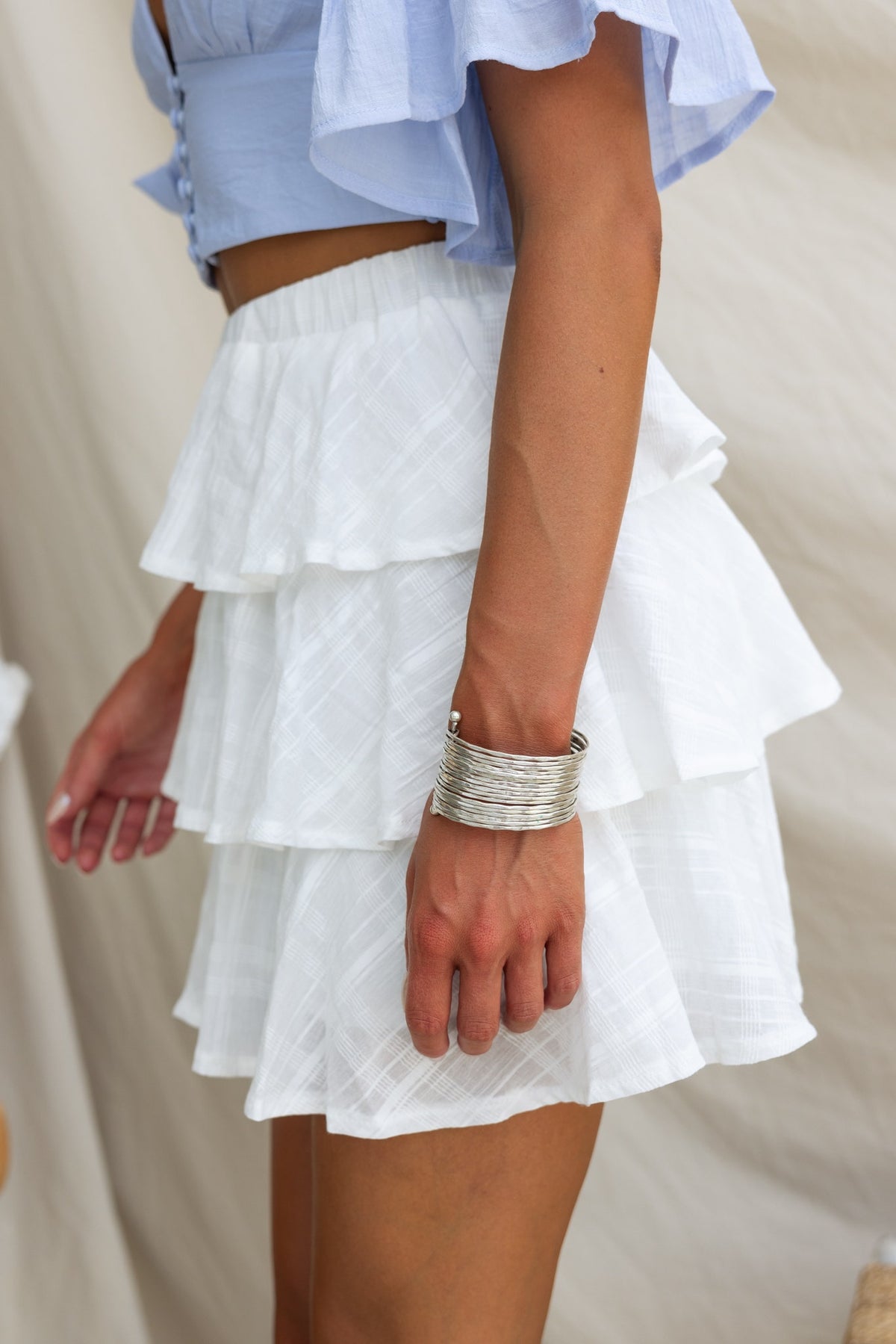 Model wearing a tiered white Madoni Skirt with a textured design, paired with a light blue cropped top.