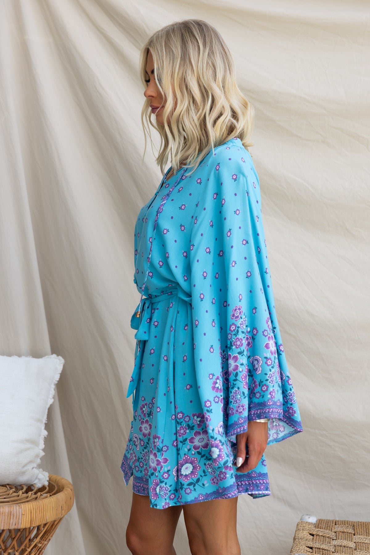 Model wearing the Nolla Dress in blue with floral patterns, featuring wide sleeves and a tie detail at the neckline.