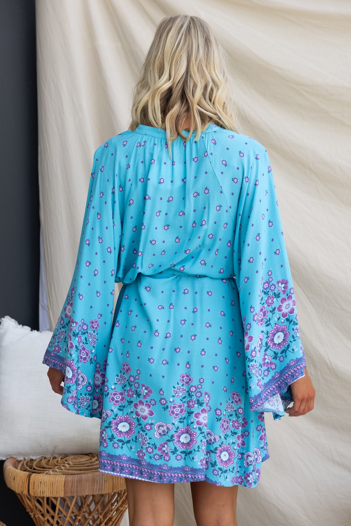 Back view of the Nolla Dress in blue with floral patterns, featuring wide sleeves and a tie detail.