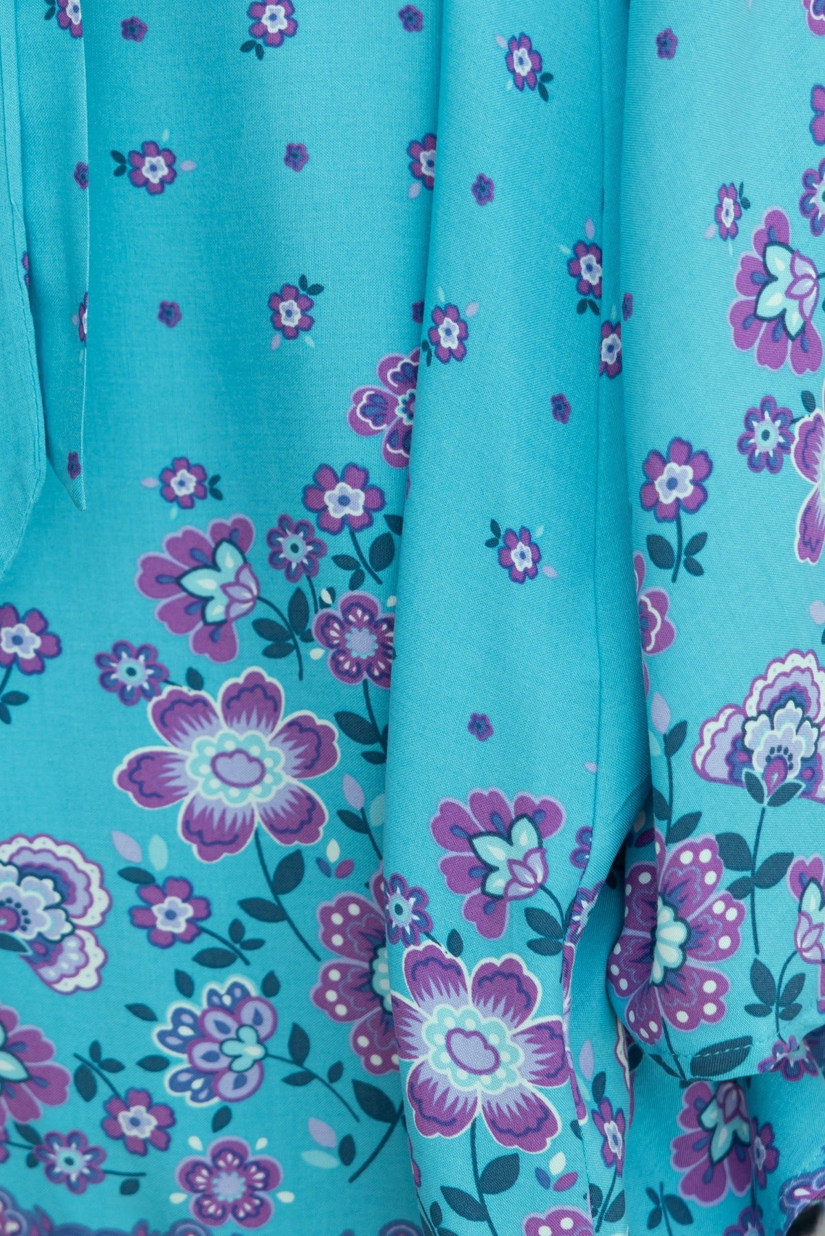 Close-up of the floral pattern on the Nolla Dress, featuring turquoise fabric with purple and white flowers.