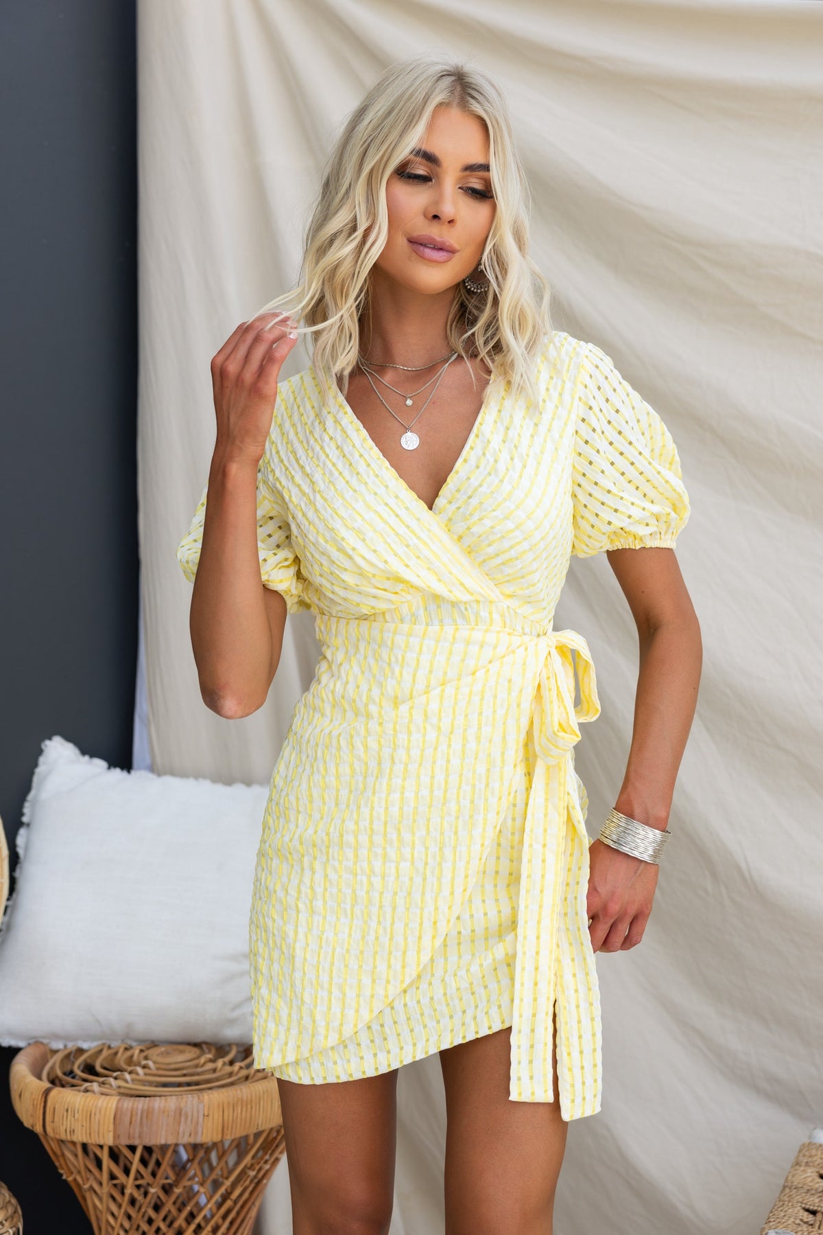 Model wearing yellow striped Thora Dress featuring V-neckline and wrap tie, styled in a chic summer setting.