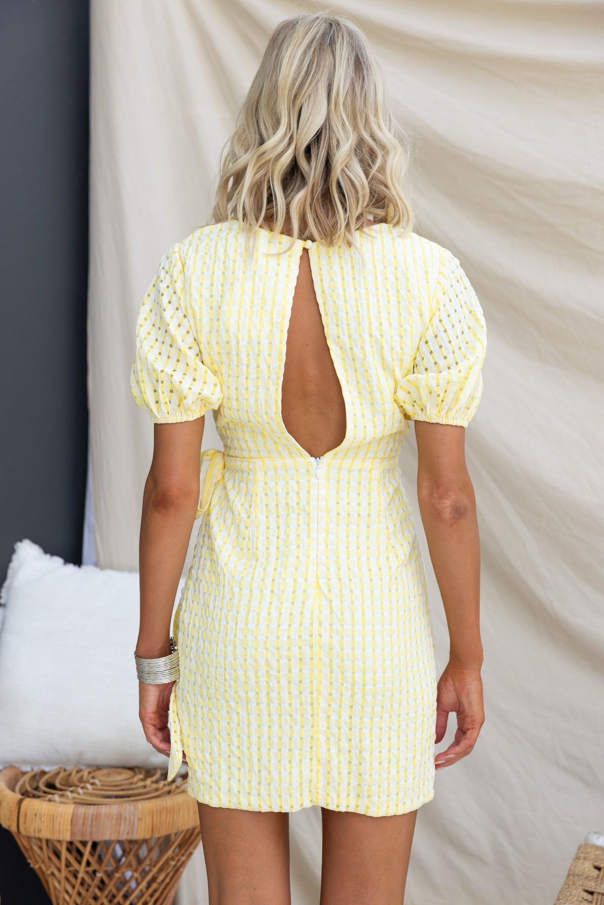 Back view of the Thora Dress featuring a V-neckline, puff sleeves, and a tie waist, designed in a striped yellow fabric.