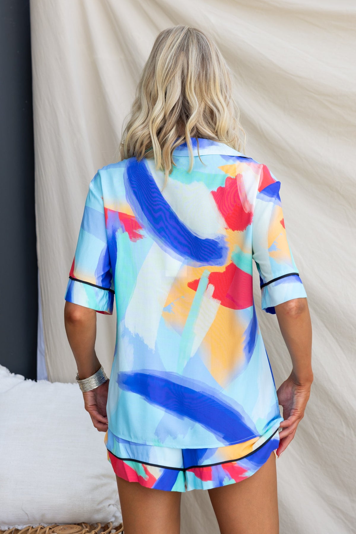 Back view of a woman in a colorful printed Focus shirt, showcasing vibrant brushstroke patterns on a light fabric.