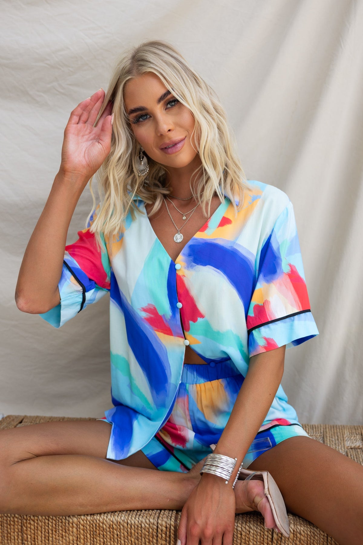 A woman wearing a colorful print Focus Shirt, featuring a button-up front and relaxed fit, sitting casually on a woven surface.