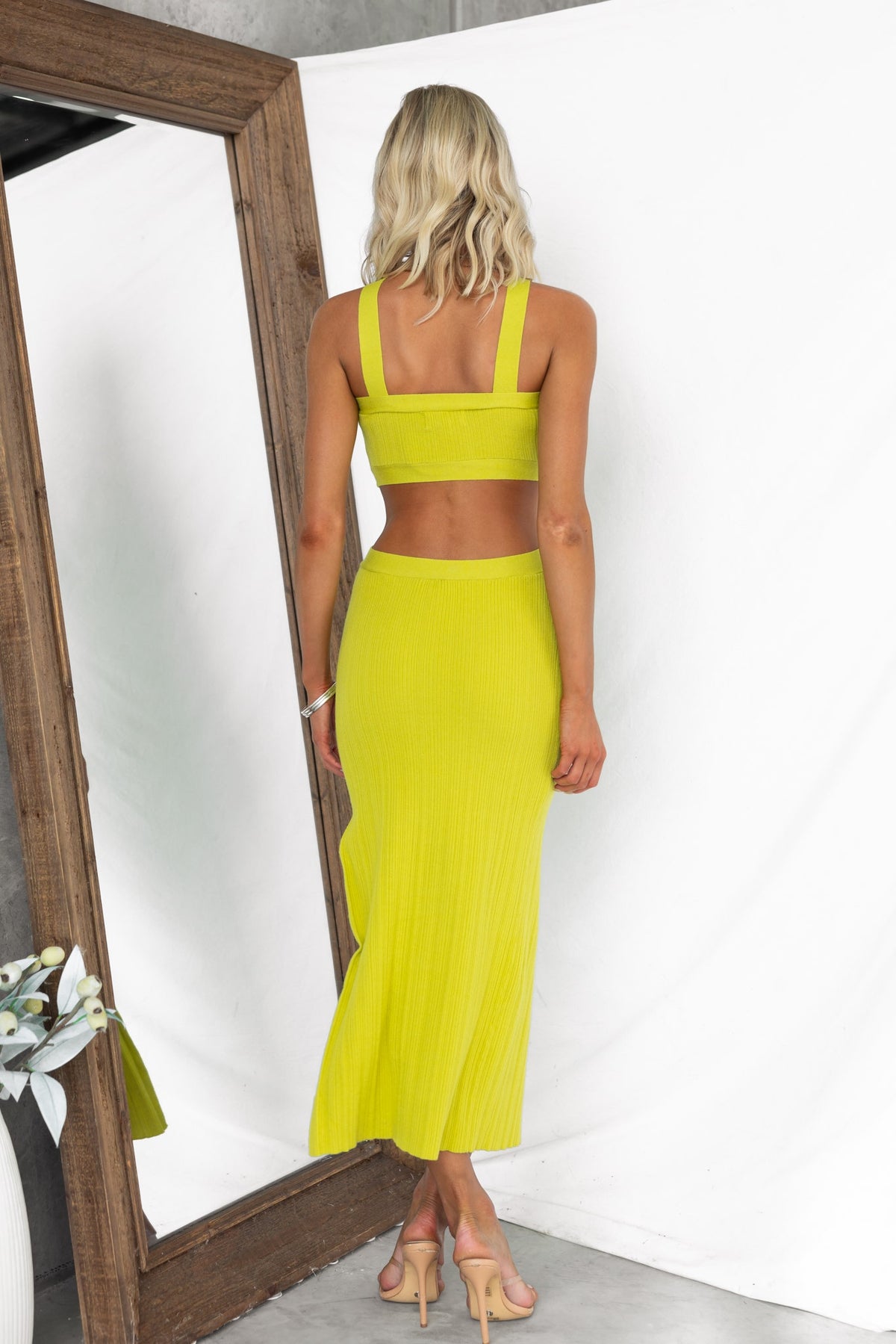 Back view of a model wearing the Oura Midi Dress in bright yellow, showcasing its ribbed design and strappy details.