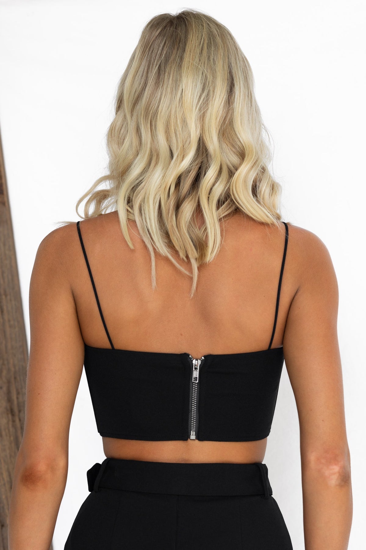 Back view of the Verde Top, a fitted black crop with thin straps and a zipper closure.