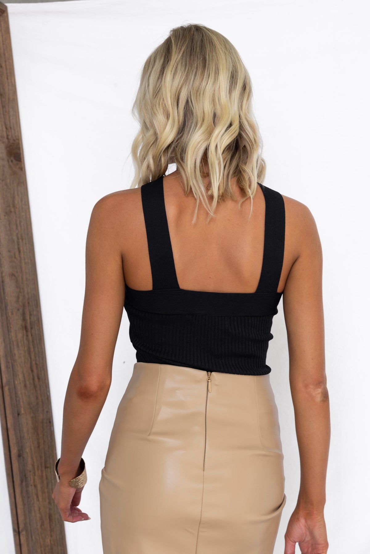 Model wearing a black ribbed knit halter top with minimalistic design and back view, paired with a beige skirt.