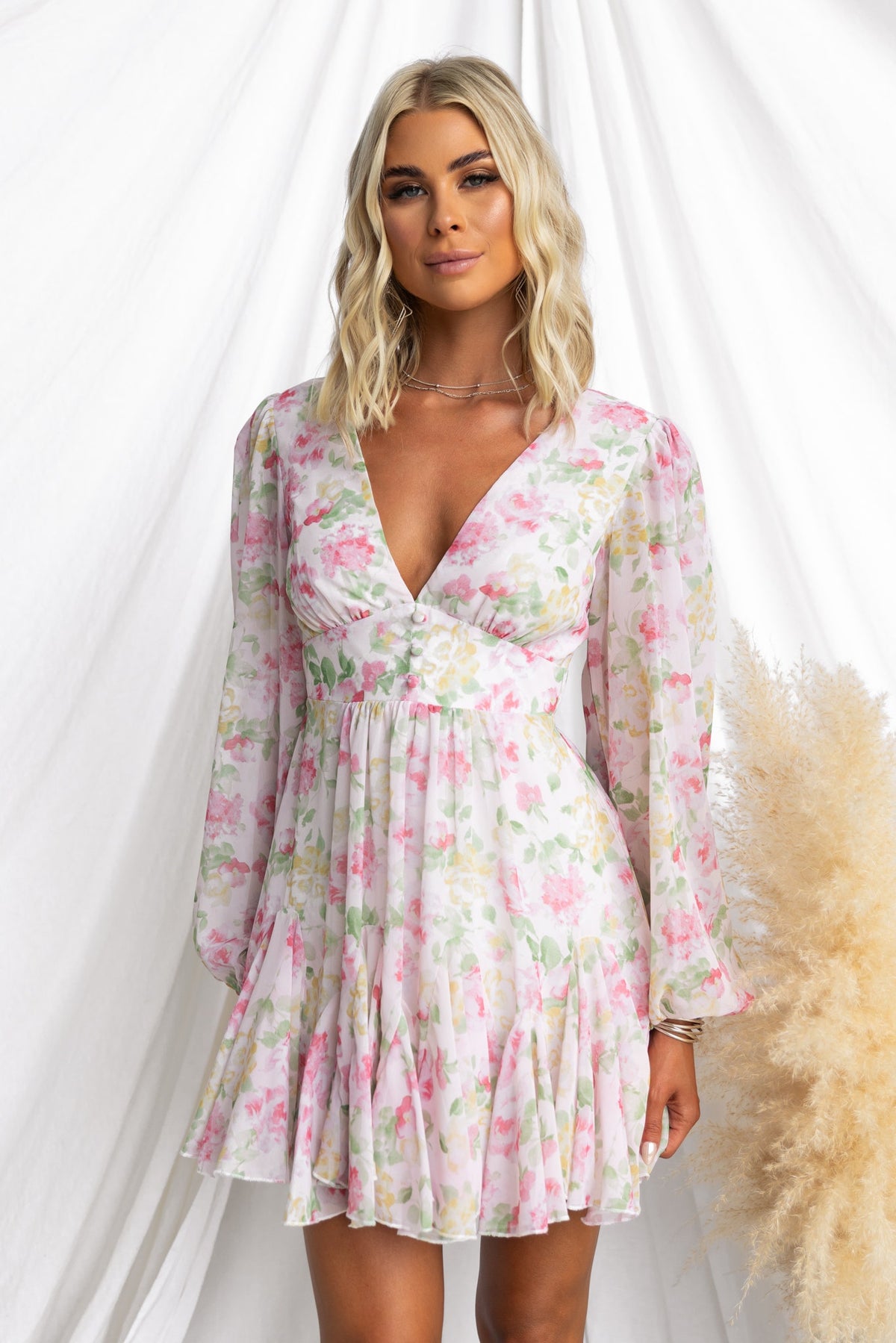 Model wearing floral Kersty Dress with V-neckline and puff sleeves, styled on a neutral backdrop.