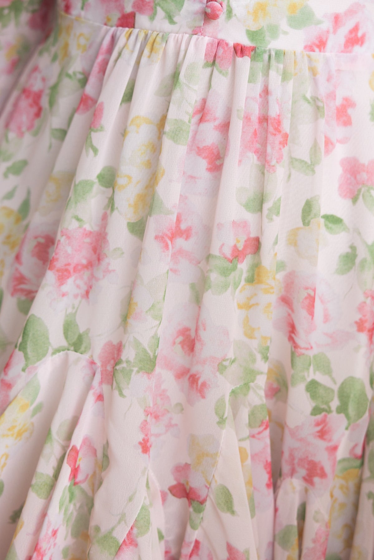 Close-up of floral chiffon dress with pink and green patterns, showcasing pleats and soft fabric texture.