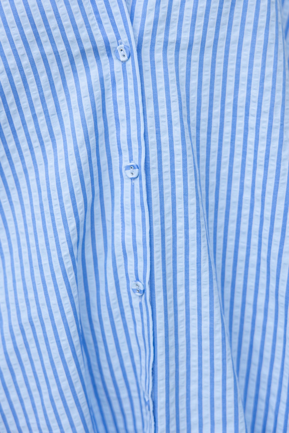 Close-up of a blue striped shirt featuring button-up front and collar detail, showcasing textured fabric.