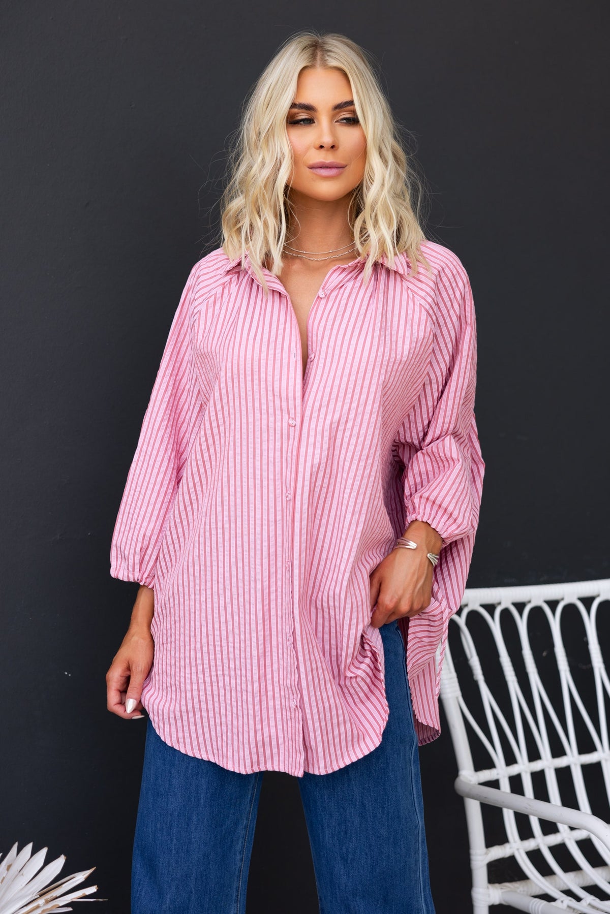 Oversized pink striped sorbet shirt with button-up front and tie detail at sleeves, styled with denim pants.