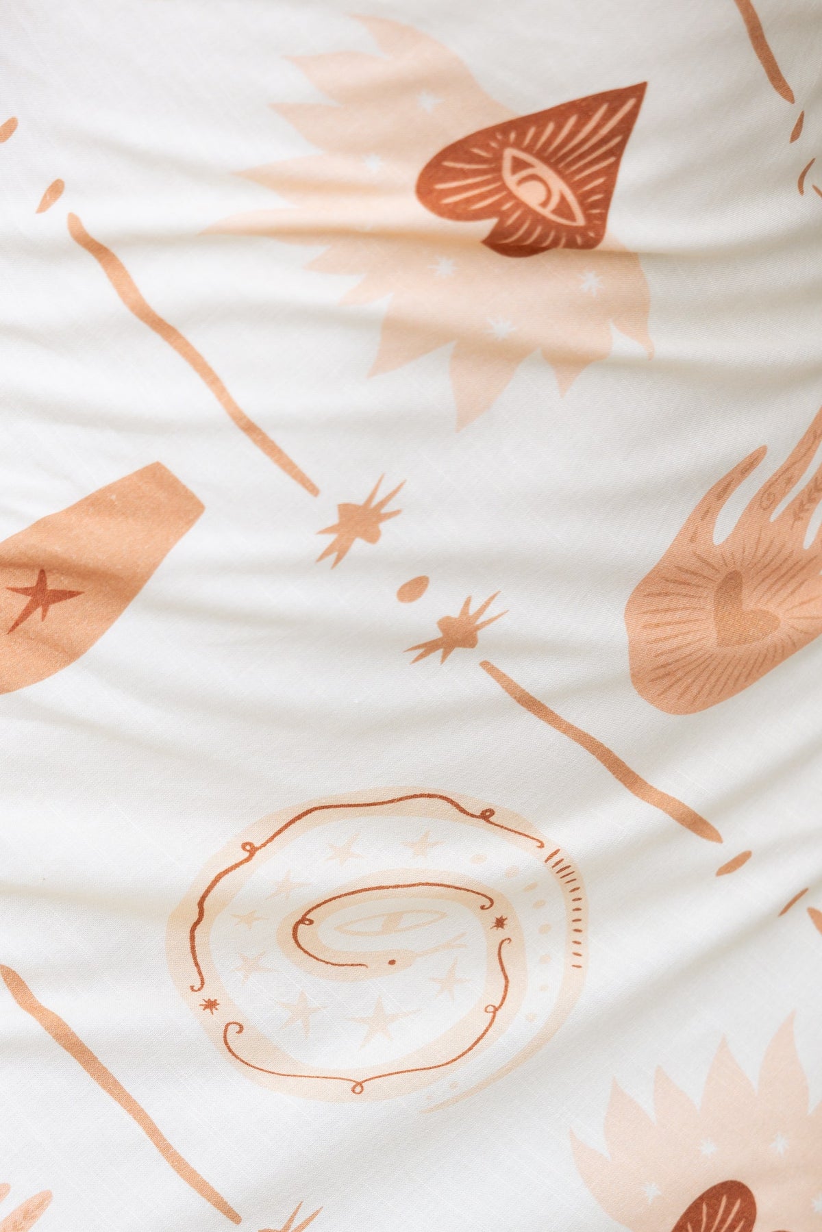 Close-up of fabric featuring warm-toned artistic prints on a cream background.