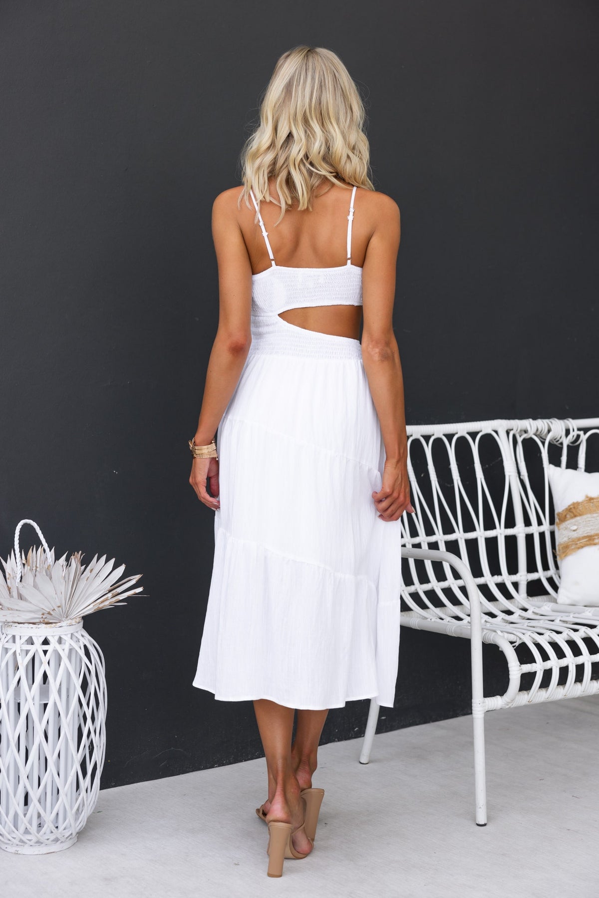 Back view of a woman in a white Panama Midi Dress featuring adjustable straps and cut-out details, styled with a boho chair.