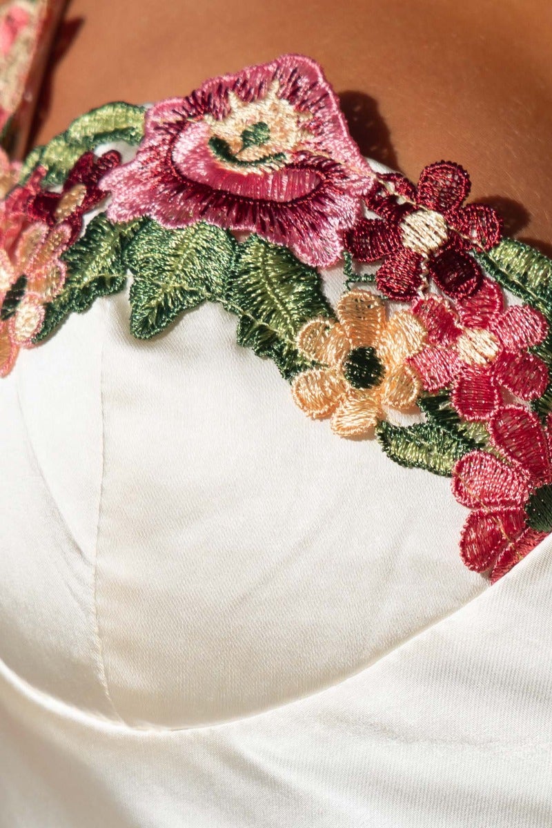 Close-up of embroidered floral trim on satin dress, featuring vibrant flowers and intricate detailing.