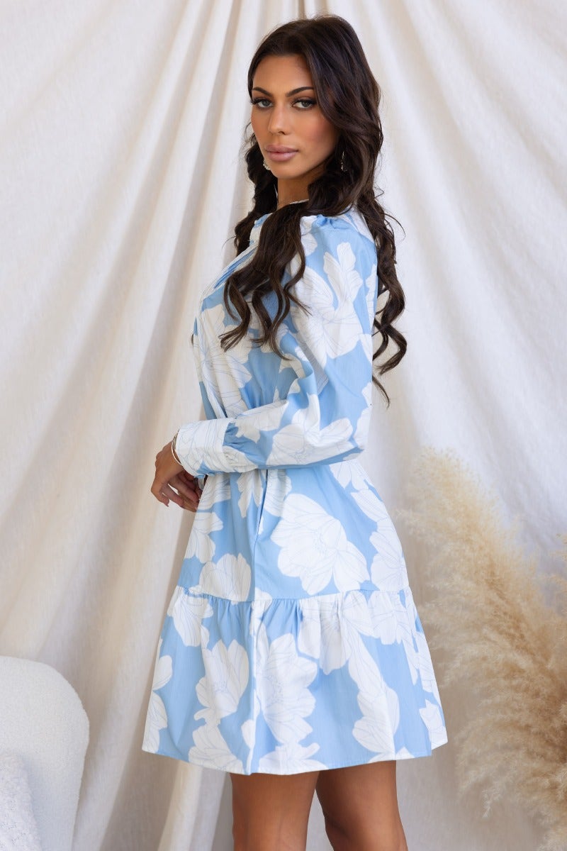 Model wearing a floral print Mellow Dress in blue with round neckline and button-up front, showcasing its stylish design.