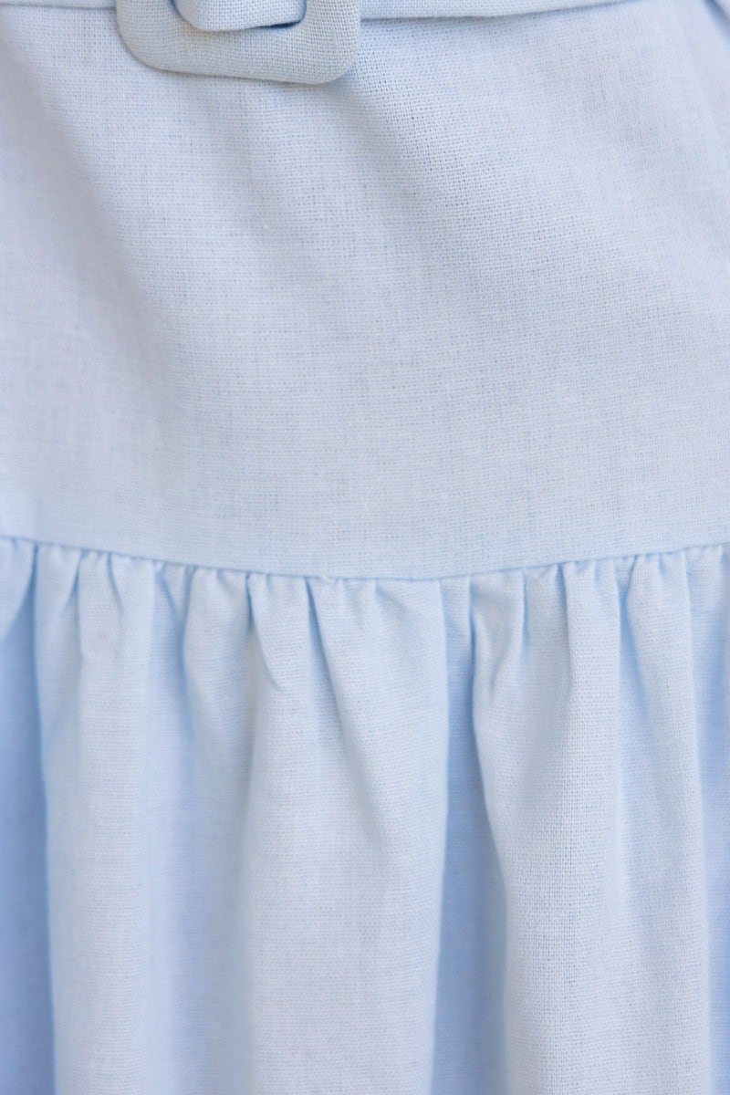 Close-up of a light blue linen blend midi dress featuring pleats and a removable fabric belt.