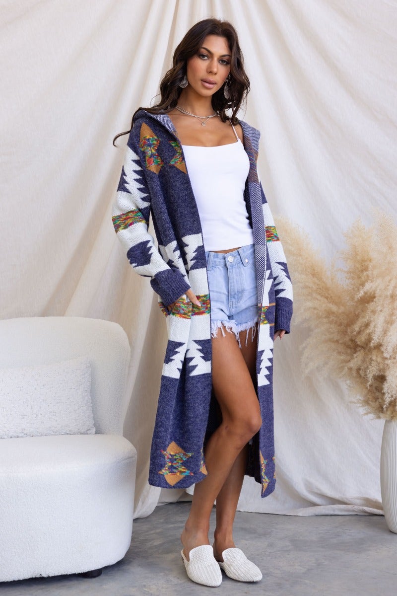 Model wearing a longline navy patterned cardigan with hood, styled with a white tank and denim shorts.