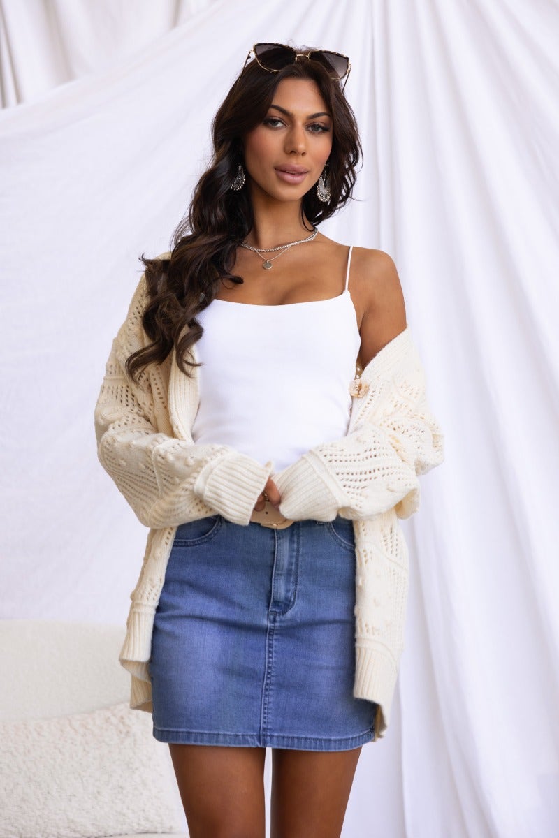 Model wearing Azaria Cardigan, a textured knit cardigan with V-neckline, styled over a white top and denim skirt.