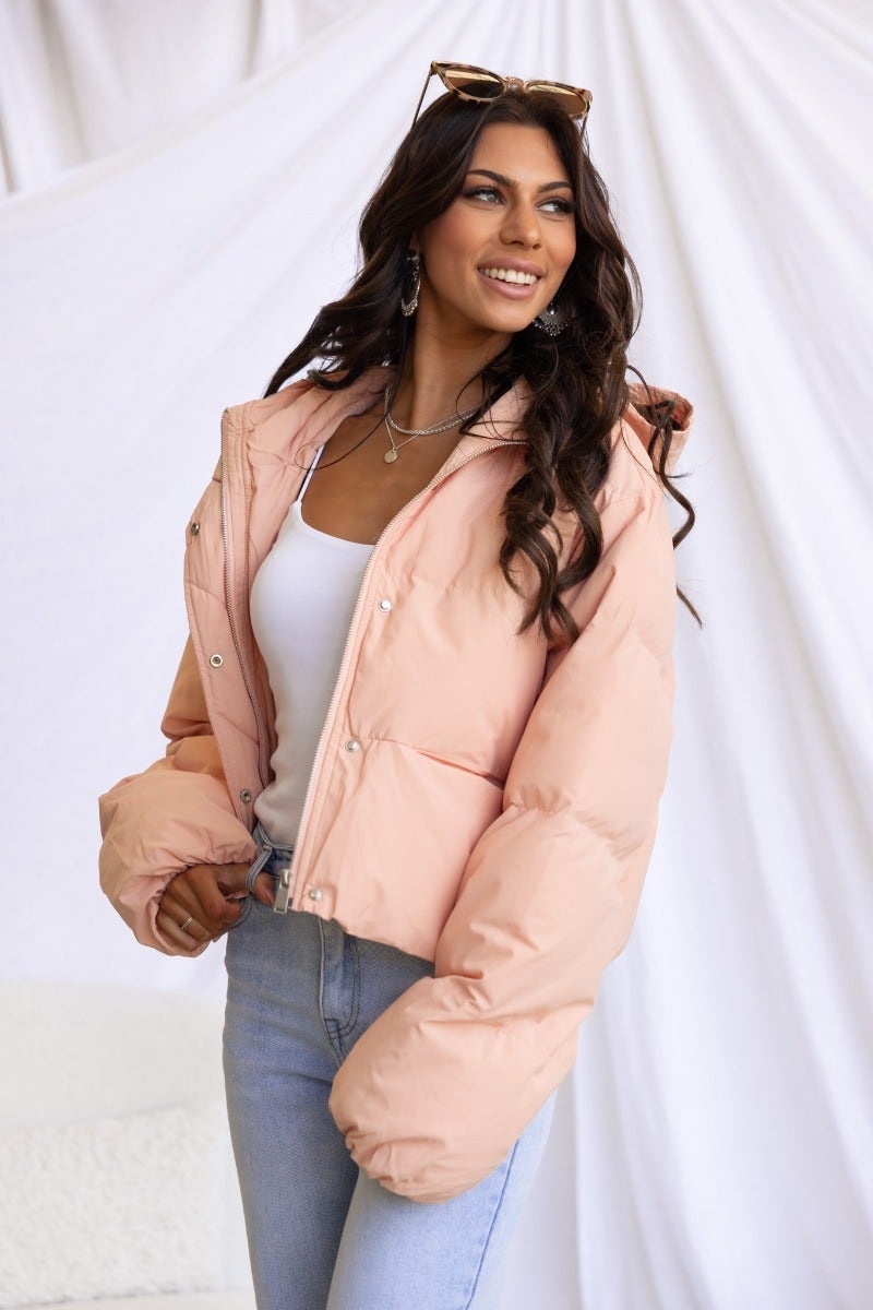 Model wearing the Vinna Puffer Jacket in pastel pink, styled with a white top and jeans, against a soft backdrop.