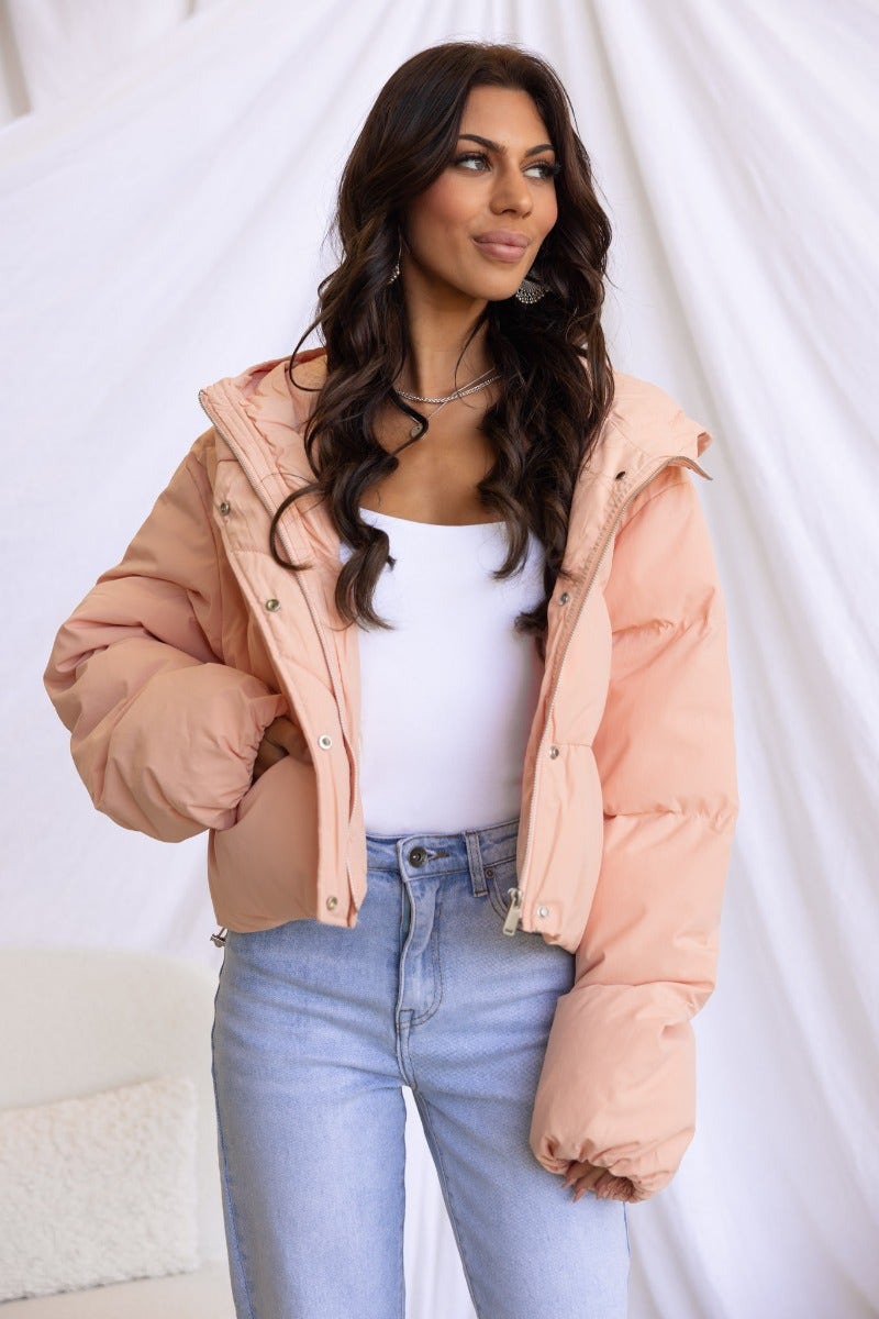 Model wearing a stylish Vinna Puffer Jacket in soft peach color, paired with light blue jeans.