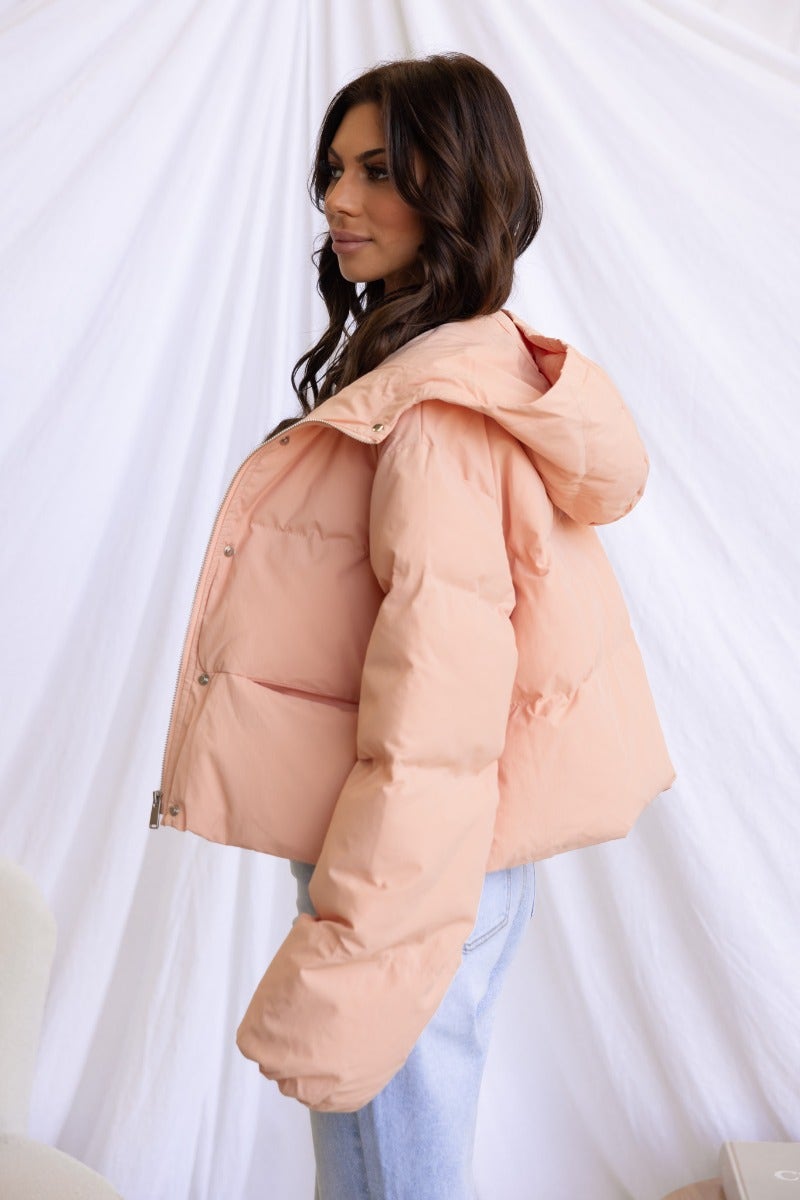 Profile view of a woman wearing a light pink Vinna Puffer Jacket, styled with casual jeans, against a soft white background.