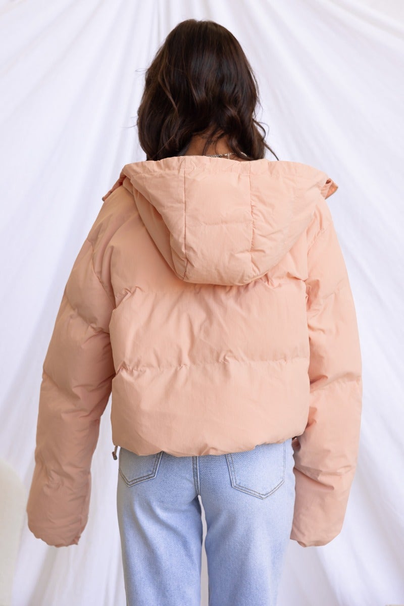 Back view of a model wearing a peach-colored Vinna Puffer Jacket paired with light blue jeans.