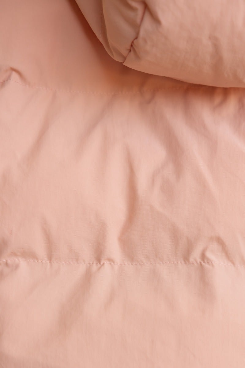 Close-up of Vinna Puffer Jacket in soft peach color, showcasing its smooth, quilted fabric texture.