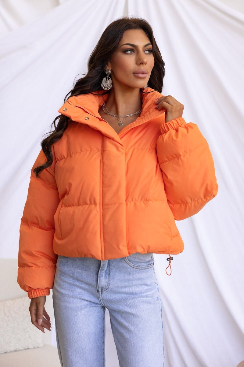 Model wearing an orange Avril Puffer Jacket with a high neckline and adjustable drawstring hem.
