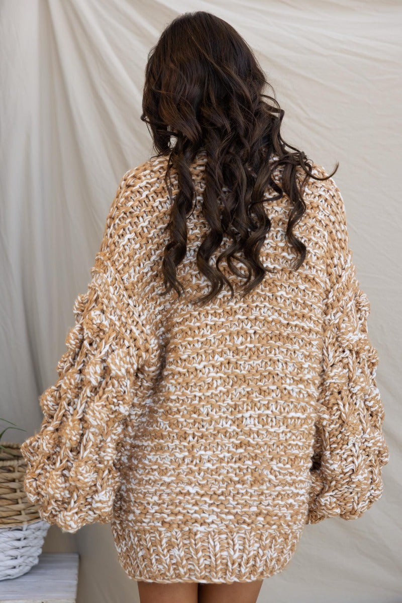 Back view of a chunky tan and cream cable knit cardigan with textured sleeves, showcasing a relaxed fit.