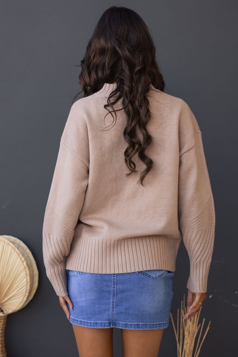Back view of a woman wearing a beige ribbed knit Cuba jumper, styled with a denim skirt.