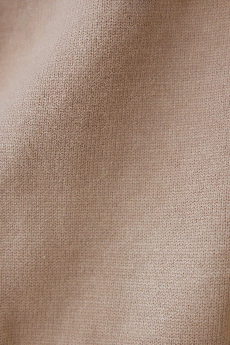 Close-up of soft, ribbed knit fabric in a light beige color, showcasing its stretch and texture.