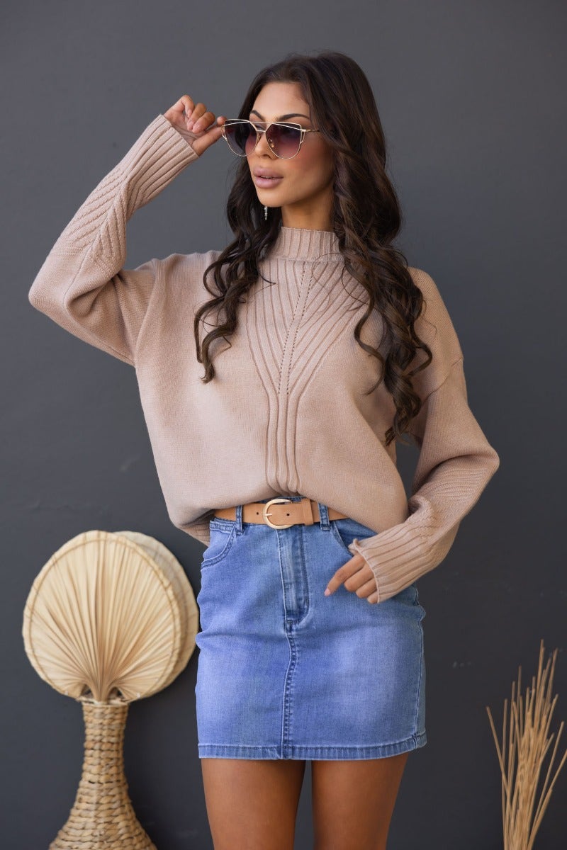 Woman wearing a beige ribbed knit Cuba jumper with a mock neckline, styled with a denim skirt and sunglasses.