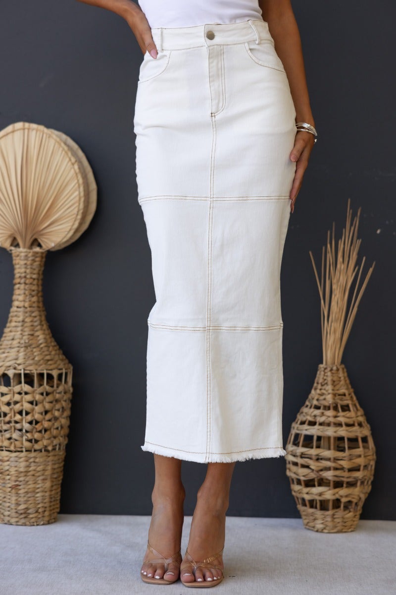 Model wearing Caria Denim Midi Skirt in cream, showcasing mid-high waist, frayed hem, and stylish fit.