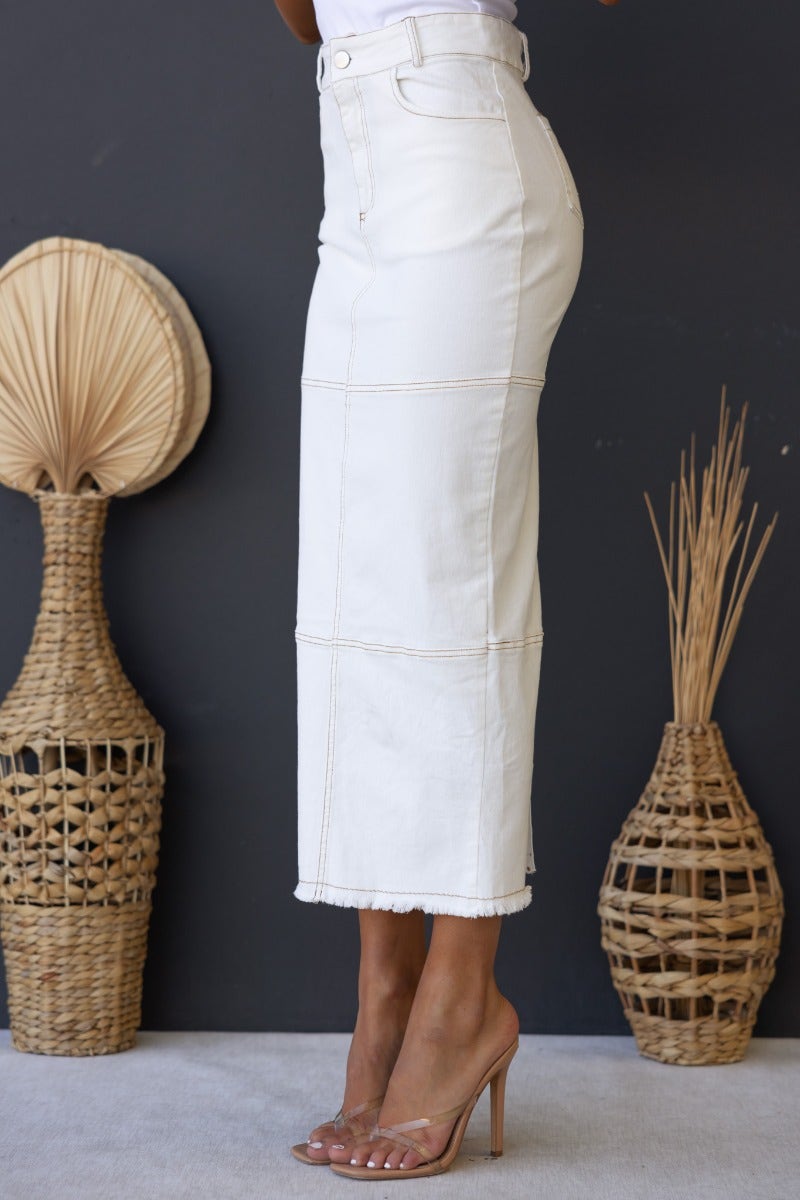 Profile view of Caria Denim Midi Skirt, showcasing mid-high waist, frayed hemline, and front/back pockets.