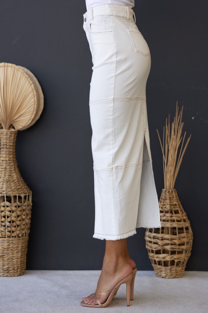 Side view of Caria denim midi skirt with frayed hem, high waist, and split design, styled with heels.