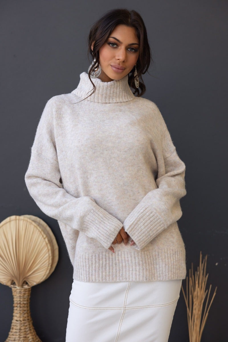 Orion Jumper in soft beige with ribbed knit, turtle neckline, and relaxed fit, styled with a white skirt.