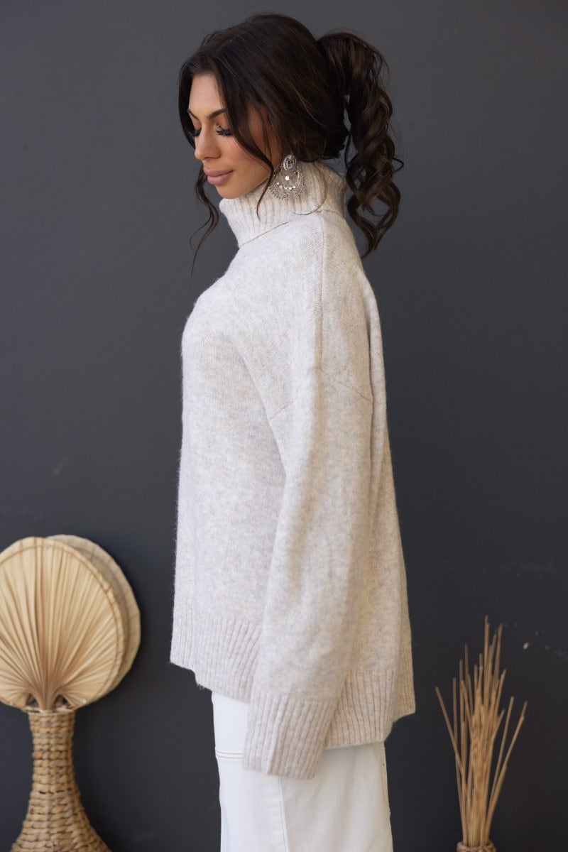 Side view of a woman wearing a ribbed knit Orion Jumper with turtle neckline, styled with white pants.