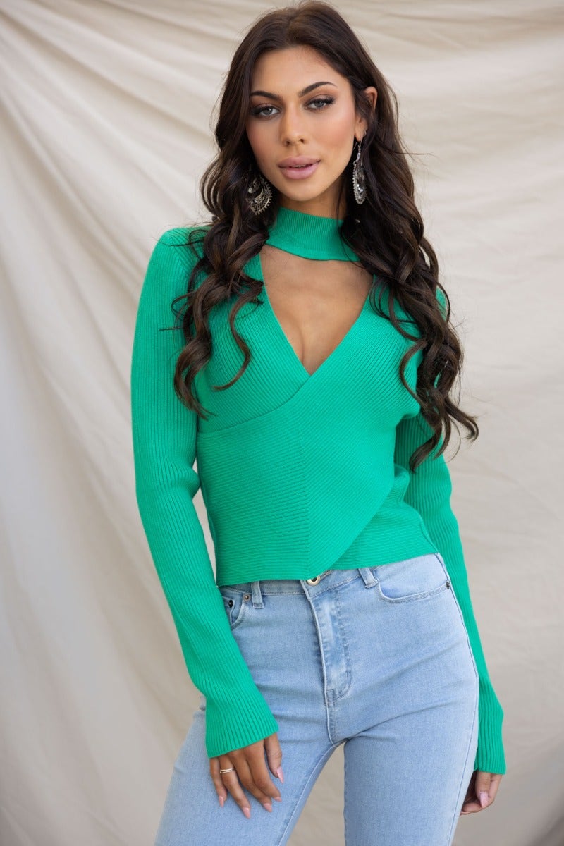 Inala Top: ribbed knit green top with high neckline and cross-over detail, styled with blue jeans.