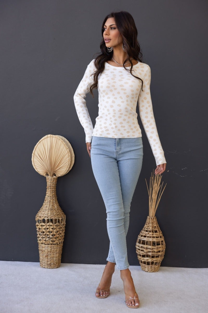 Model wearing a cream ribbed knit Greyson top with round neckline and light blue skinny jeans, styled with decorative baskets.