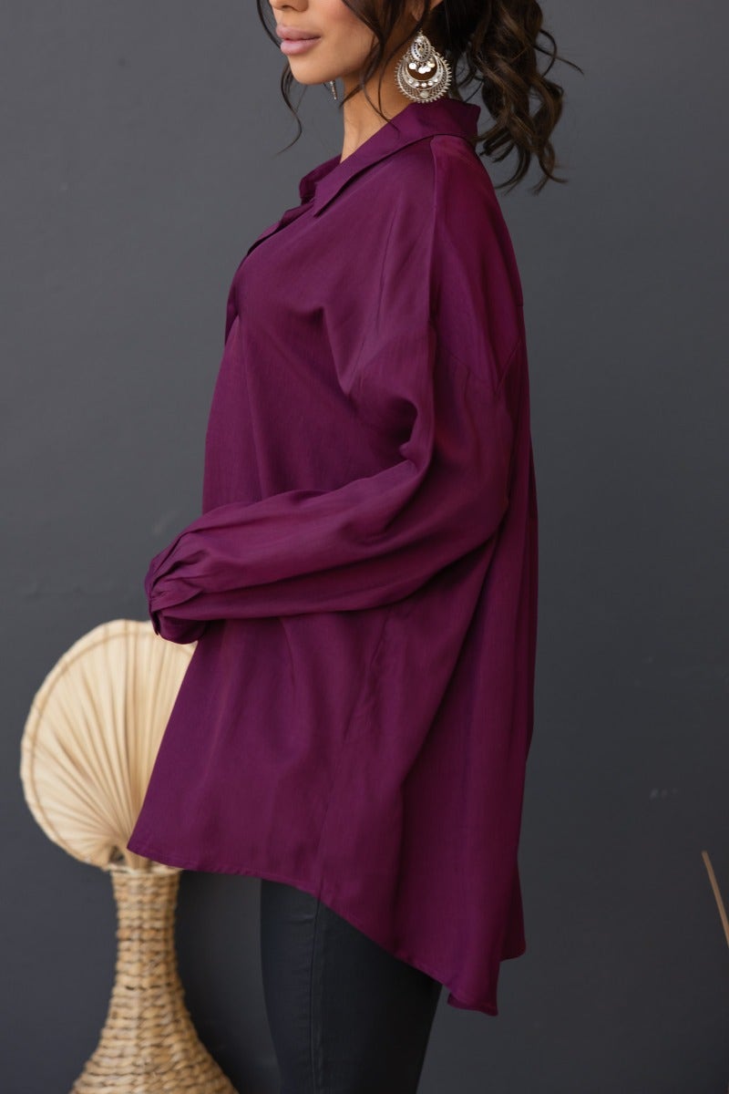 Satin nori top in deep purple, featuring a relaxed fit and button-up front, styled with statement earrings.